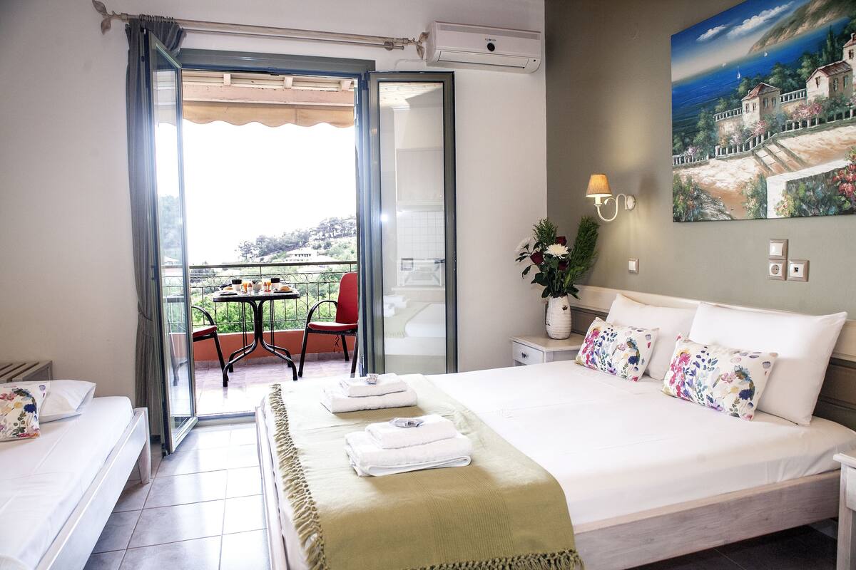 A hotel room with a bed, a balcony with a table and chairs, and a painting on the wall.