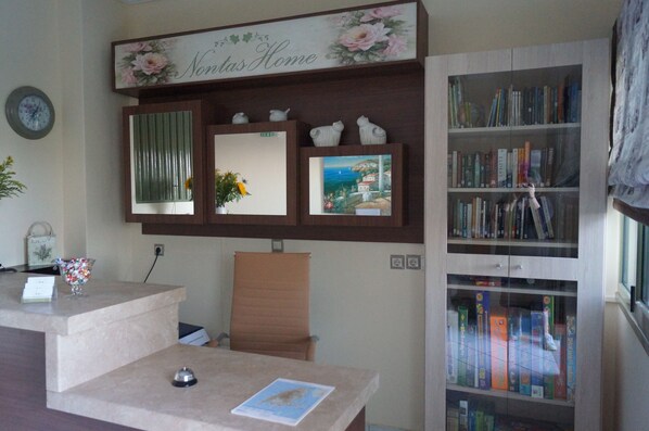 A reception desk with a clock, a floral sign above it, a bookshelf, and a chair. - Nontas Home (Lefkada)
