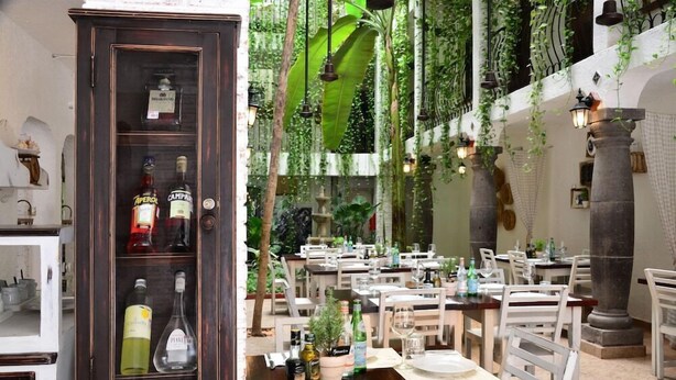 A restaurant with a dark wooden cabinet displaying liquor bottles, white chairs, and tables set for dining. - Unic Design Hotel (Playa del Carmen)
