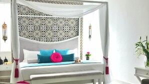 A four-poster bed with a patterned headboard, a bedside table with a lamp, and a potted plant. - Unic Design Hotel (Playa del Carmen)