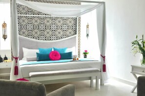 A four-poster bed with a patterned headboard, a bedside table with a lamp, and a potted plant. - Unic Design Hotel (Playa del Carmen)