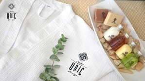 A white towel with a logo and text, a small plant, and a box of toiletries. - Unic Design Hotel (Playa del Carmen)
