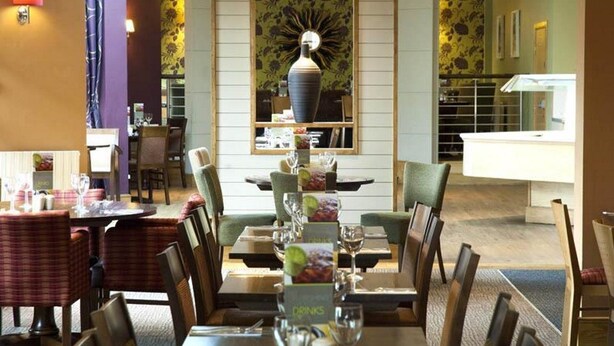 A restaurant with tables set for dining, a central decorative vase, and a counter area. - Premier Inn Leicester Fosse Park (Leicester)