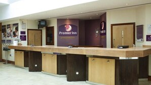 A hotel reception desk with a prominent Premier Inn sign, a reception counter, and a digital screen. - Premier Inn Leicester Fosse Park (Leicester)