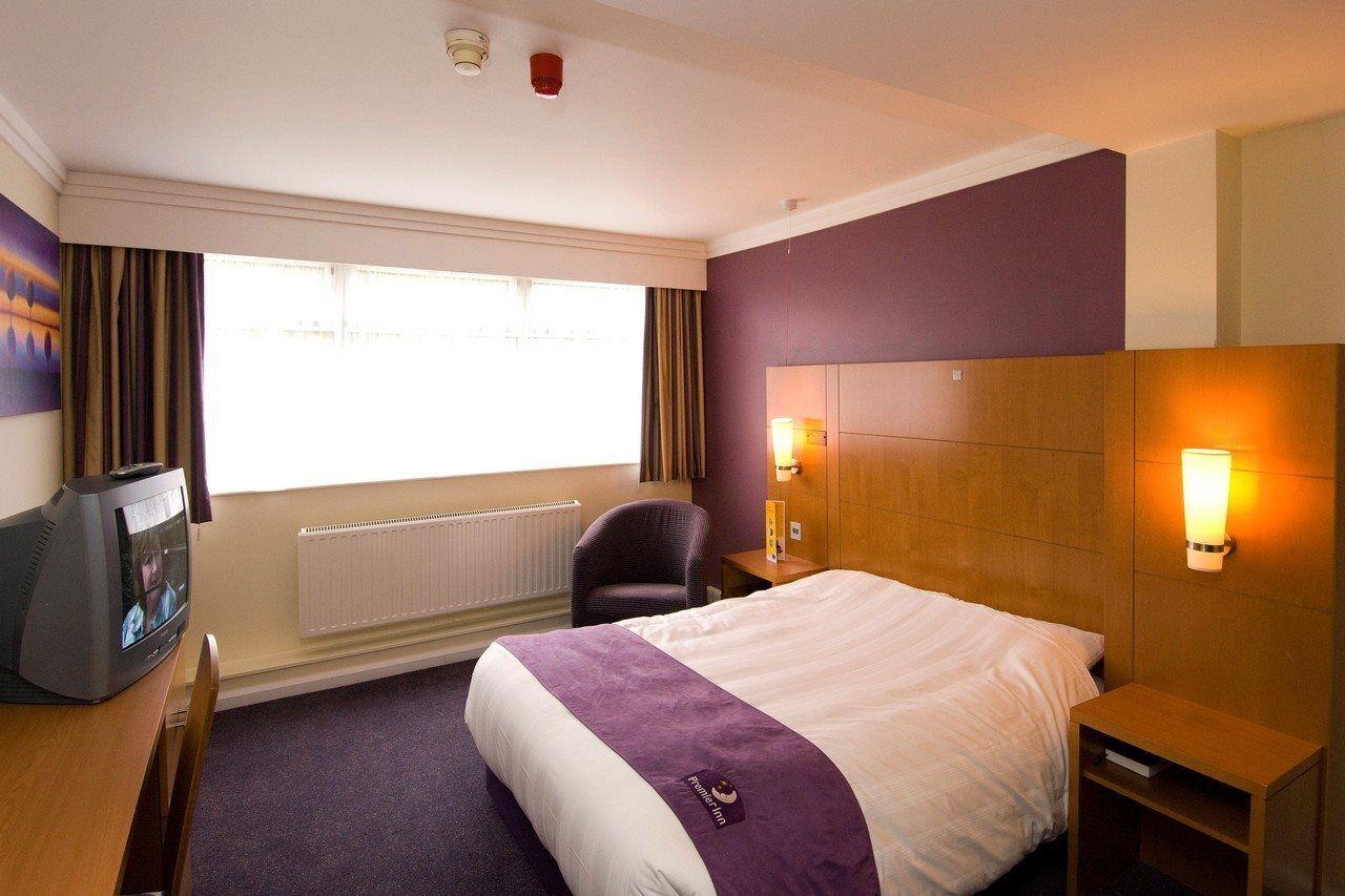 A hotel room with a bed, a desk with a television, a chair, and two wall-mounted lamps.