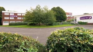 A Premier Inn hotel with a parking lot, green hedges, and a large tree in the foreground. - Premier Inn Leicester Fosse Park (Leicester)