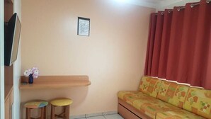 A small living area with a sofa, two stools, a small table, and a TV mounted on the wall. - Hotel Diroma Fiore. (caldas novas)