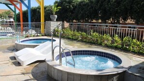 A swimming pool area with two hot tubs, a covered seating area, and a metal fence. - Hotel Diroma Fiore. (caldas novas)