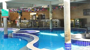 A swimming pool with blue tiles, a bar area with chairs, and a tiled wall. - Hotel Diroma Fiore. (caldas novas)