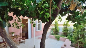 Un patio con una mesa y sillas, una planta en maceta y un pequeño jardín con arbustos y un árbol.