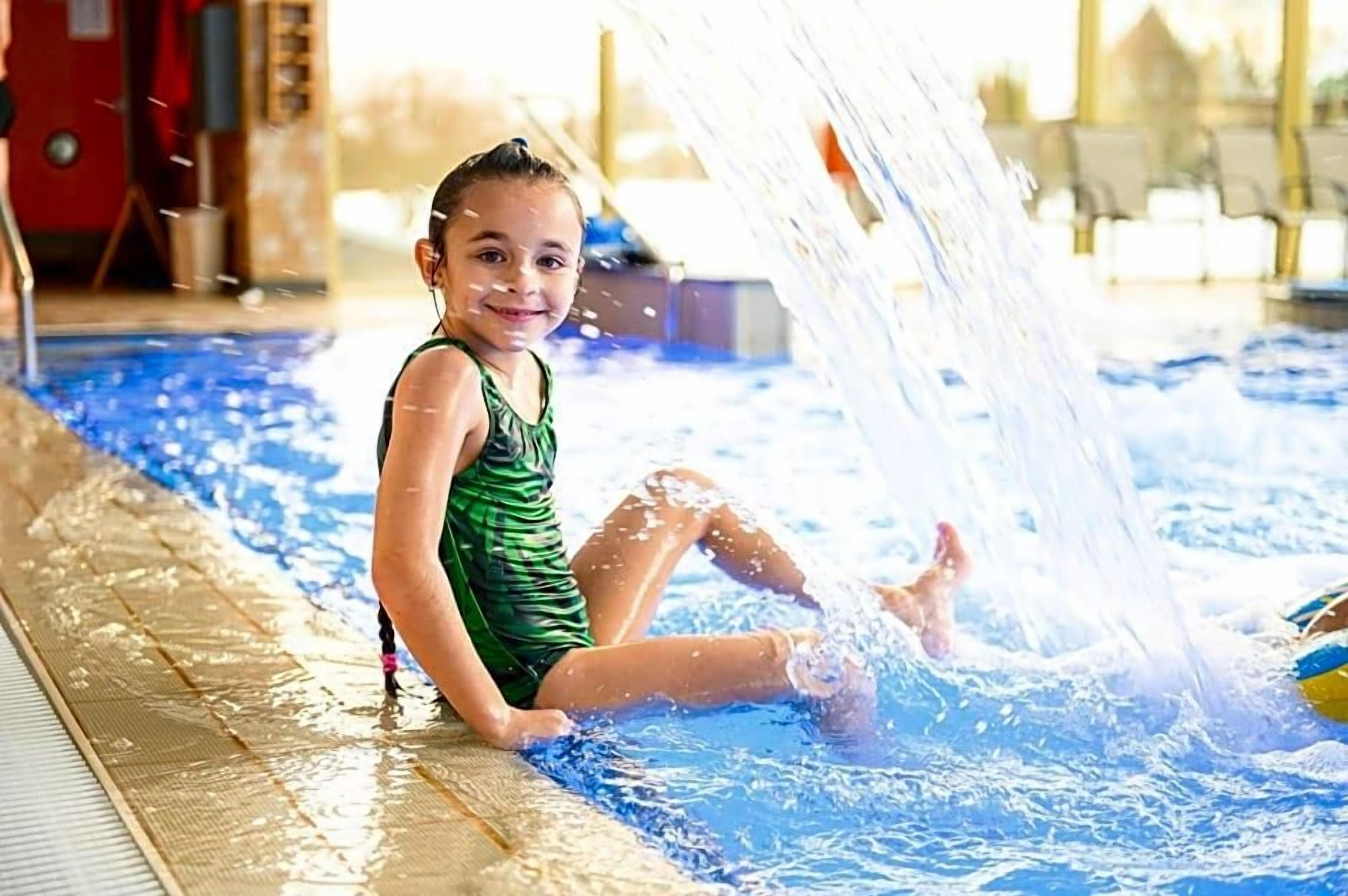 A child sitting by a pool with water splashing around.