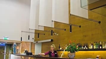 A bar area with a large digital screen displaying a nature scene, a bar counter with a plant, and a person standing behind it.