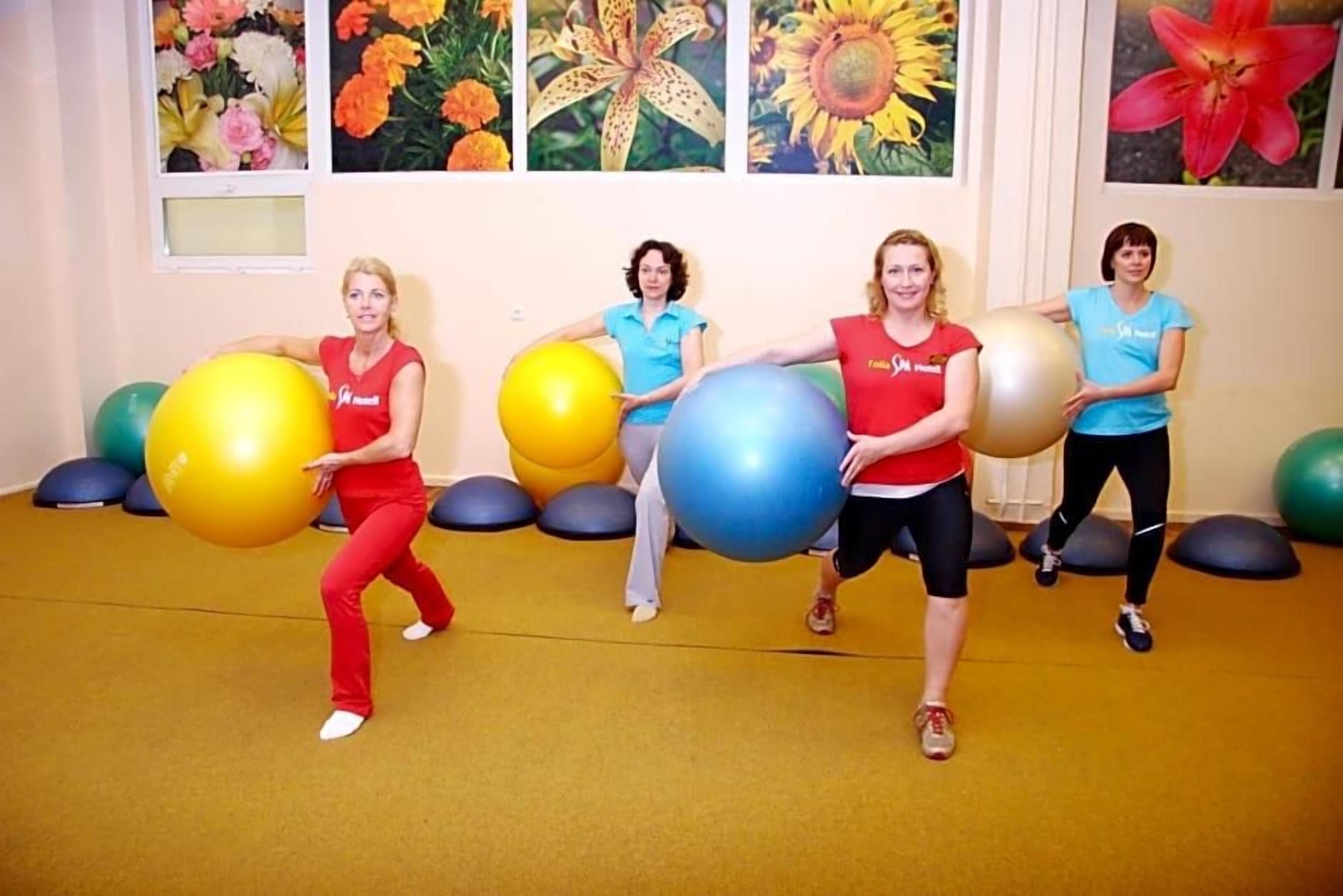 Four individuals in a room with exercise balls, a yellow carpet, and floral wall art.