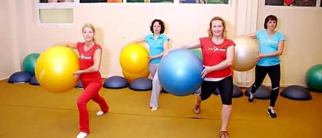 Quatro pessoas em um espaço com bolas de exercício, carpete amarelo e painéis decorativos florais.