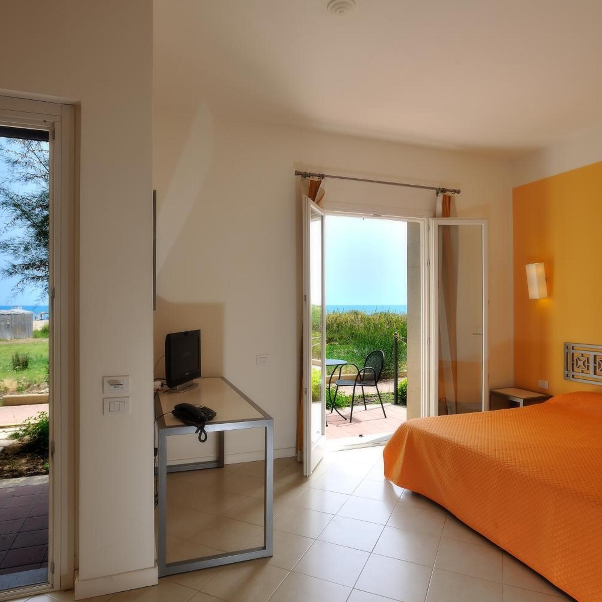A hotel room with a bed, a desk with a computer, a chair, and a view of the outdoors.