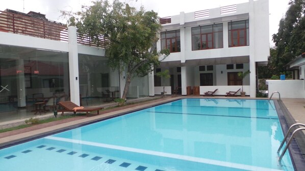 A modern building with a swimming pool, glass doors, and outdoor seating.