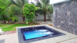 A hot tub in a garden with palm trees and a tiled wall.