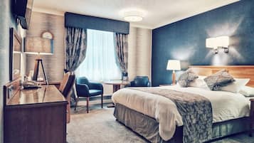A hotel room with a bed, desk, chair, and a large window with curtains.