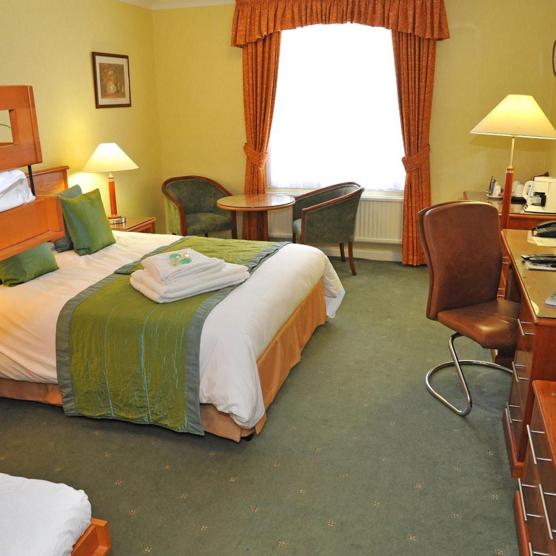 Ein Hotelzimmer mit Bett, zwei Stühlen, Schreibtisch, Lampe und einem Fenster mit Vorhängen.