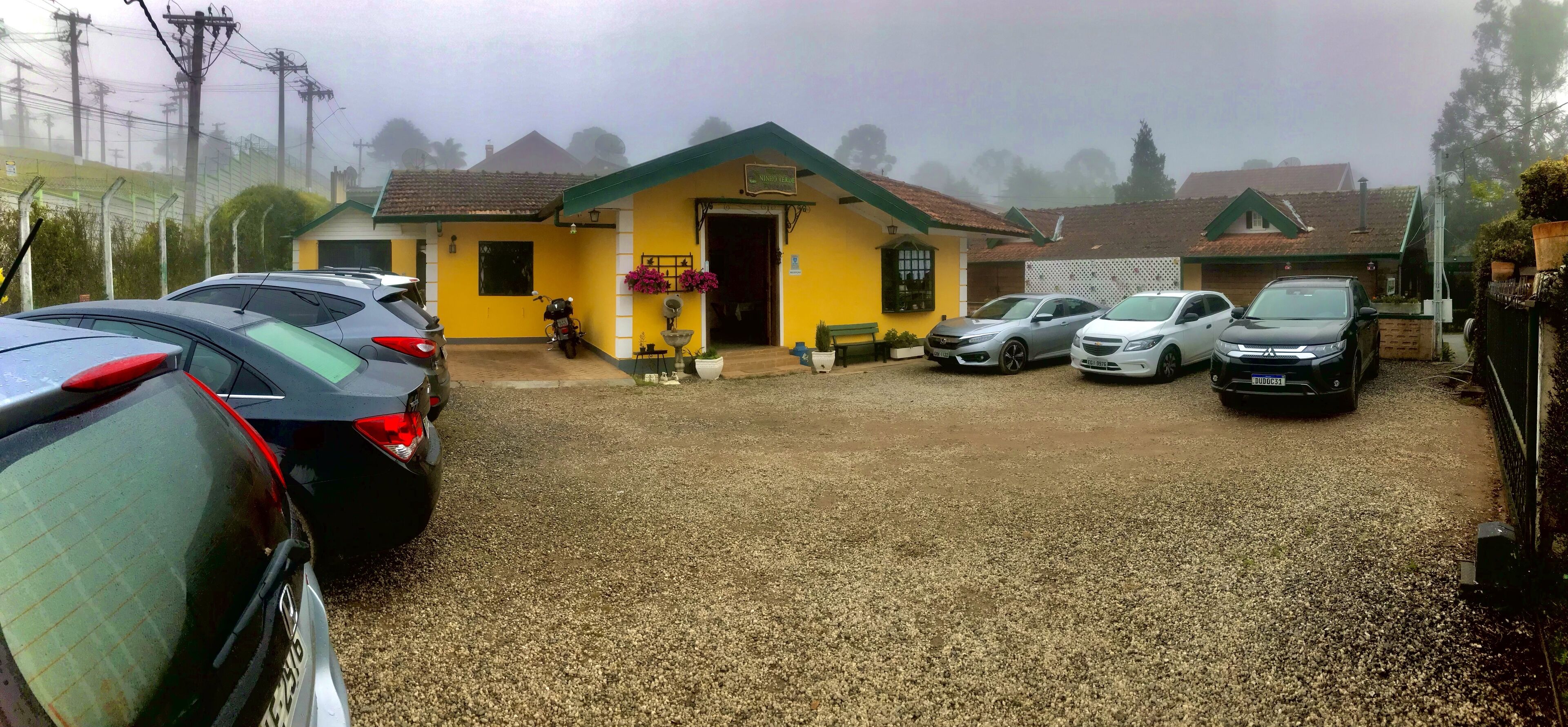 A building with a yellow facade and a gravel driveway. There are several cars parked in front.