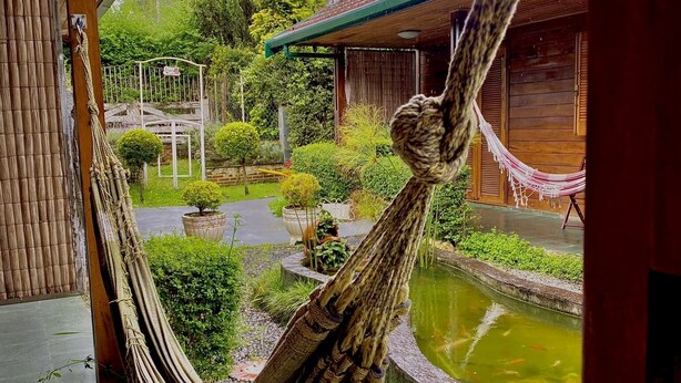 A hammock hanging over a wooden deck with a koi pond and a garden.