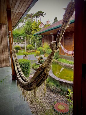 A hammock hanging over a wooden deck with a koi pond and a garden.