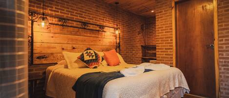 Ein Schlafzimmer mit Backsteinwand, Holzboden und einem Bett mit vielen Kissen und einer Decke.