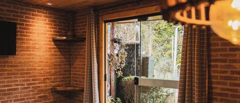 A bedroom with a wooden ceiling, brick walls, a bed with pillows, and a window with curtains.