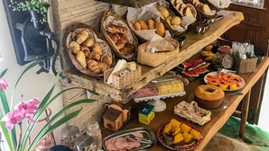 A breakfast buffet with various food items, including pastries, fruits, and beverages, set against a rustic brick wall with decorative lighting.