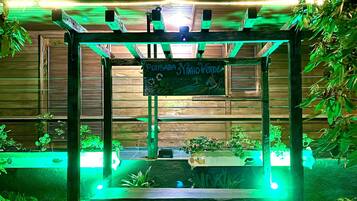 Un belvédère surmonté d’une enseigne indiquant « Pousada Nino Verde », la nuit, entouré de verdure et illuminé par des lumières vertes.