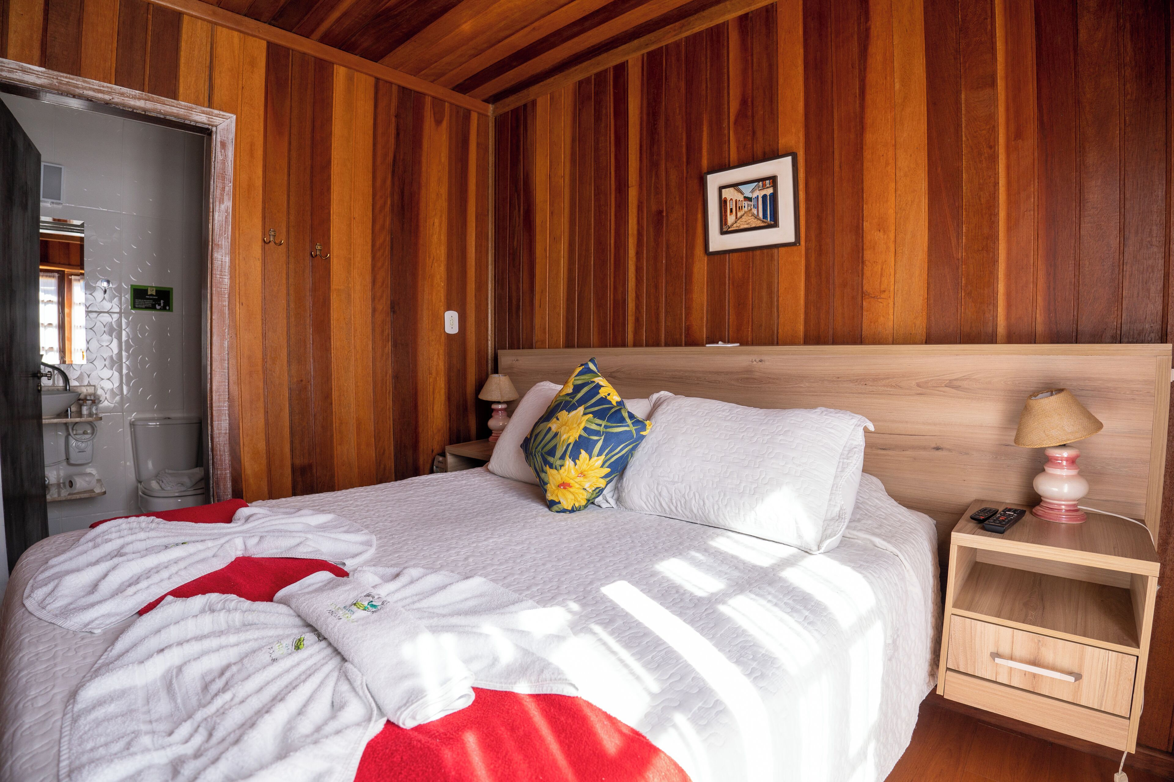 Een kamer met houten lambrisering, een bed, een nachtkastje en een aan de muur hangend schilderij.