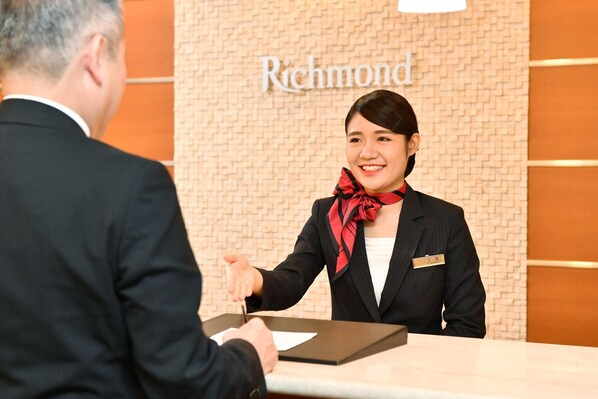 Una recepción de hotel con una recepcionista y un huésped.