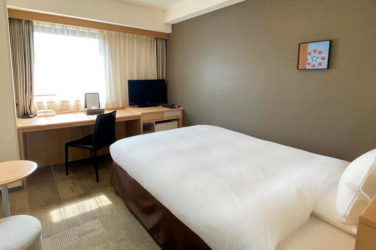 Una habitación de hotel con cama, escritorio, silla y televisor.