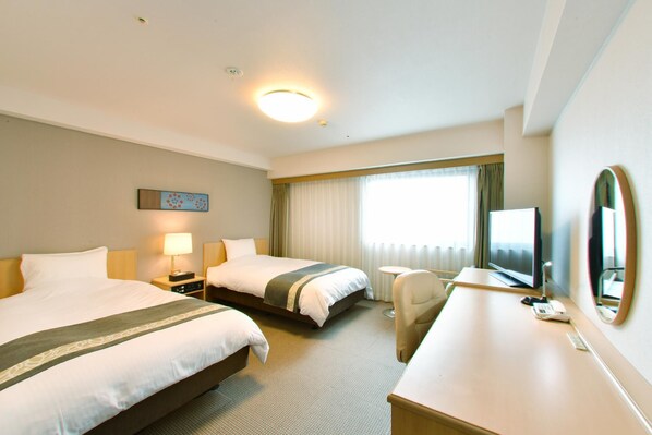 Habitación de hotel con dos camas, un escritorio, una silla, un televisor y una ventana con cortinas.