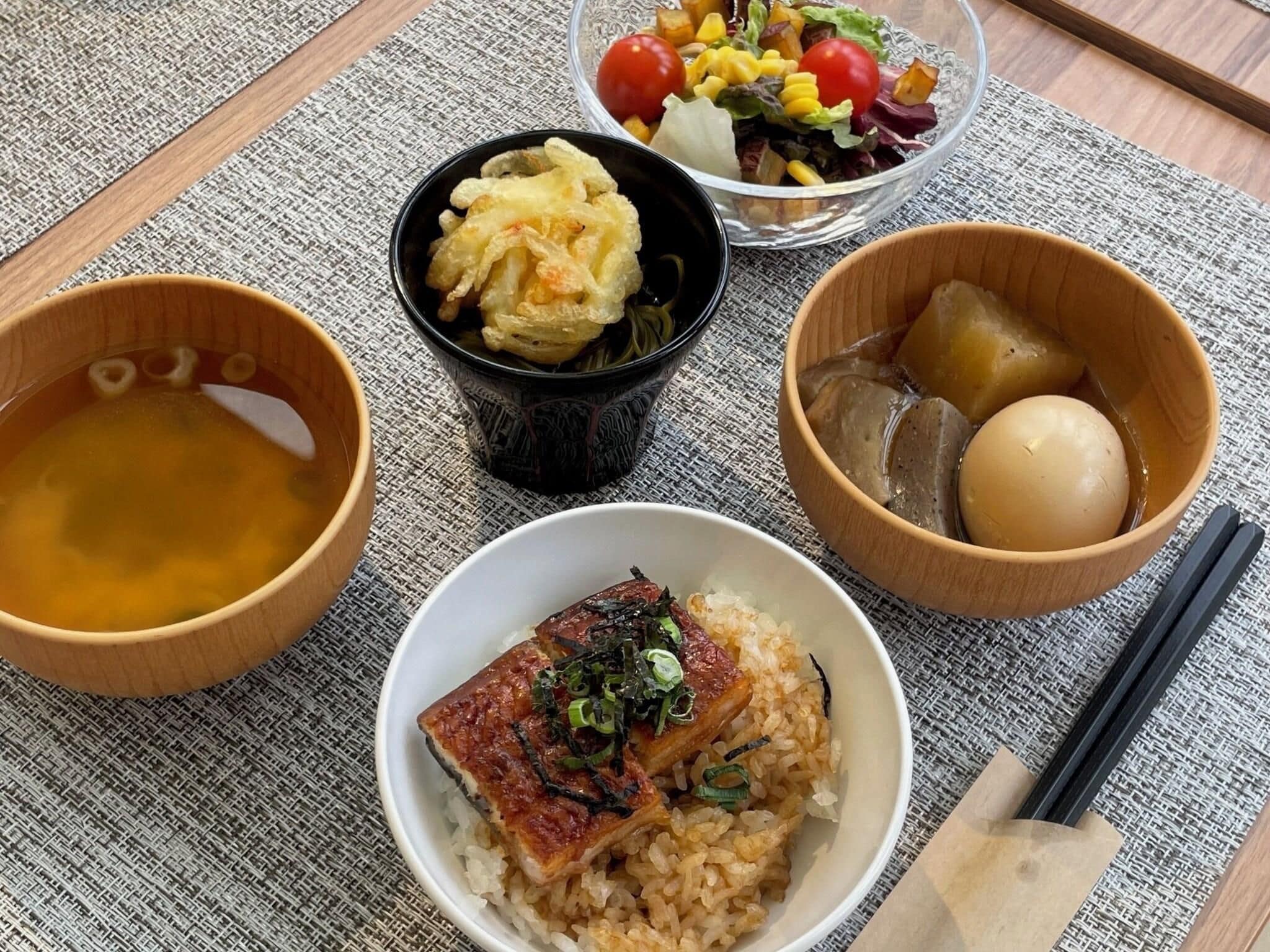 A meal with rice, fish, and vegetables on a woven mat.