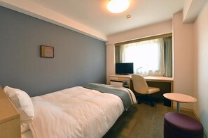 Habitación de hotel con cama, escritorio, silla y una pequeña mesa.
