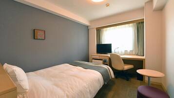 A hotel room with a bed, desk, chair, and a small table.