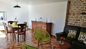 Un salon comprenant une table à manger, des chaises, un fauteuil vert, un canapé et un mur en pierre.