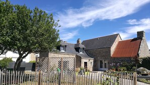 Une maison en pierre avec un toit rouge, une clôture en bois et un arbre au premier plan.