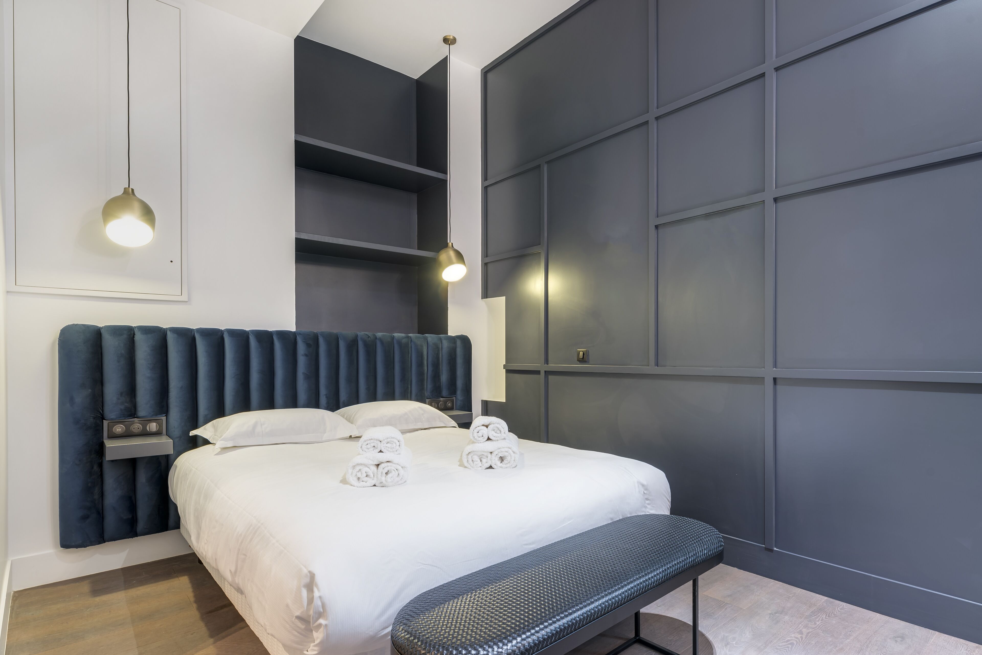 Ein modernes Hotelzimmer mit einem großen Bett, einer Bank, einem Wandregal und zwei Pendelleuchten.