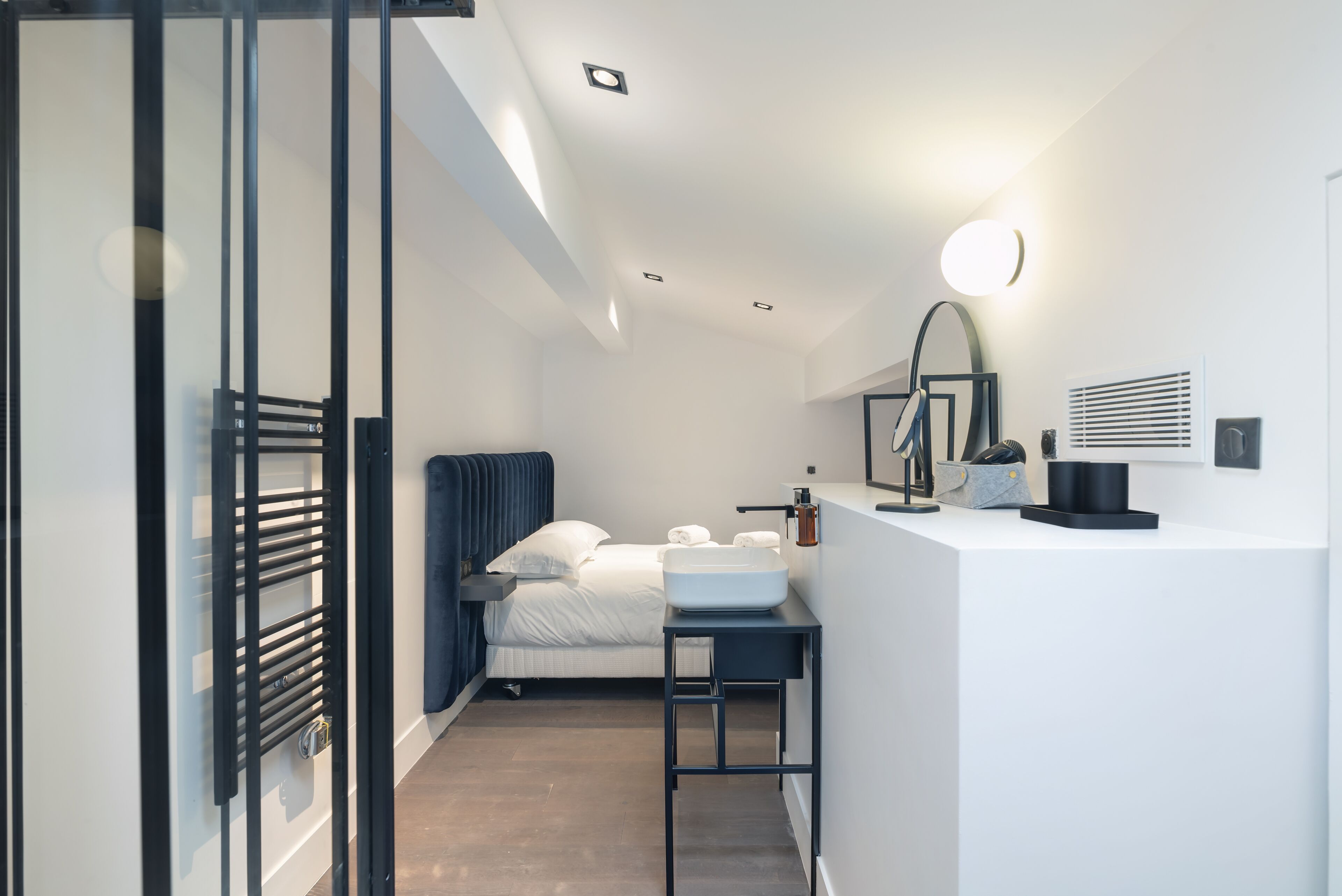 Un dormitorio moderno con cama, mesita de noche y pequeño escritorio con lavabo.