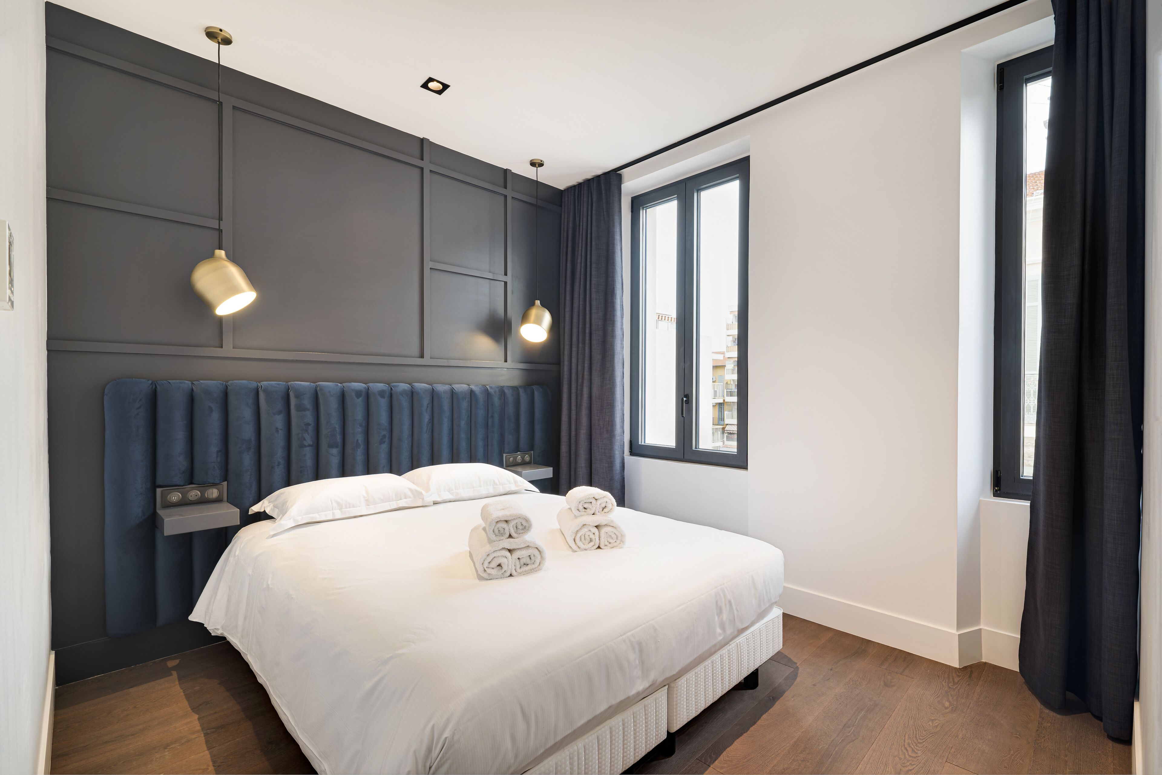A modern hotel room with a large bed, two bedside lamps, a window with curtains, and a view of the city.