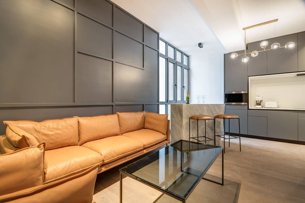 A modern living area with a leather sofa, a glass coffee table, and a kitchen with bar stools.