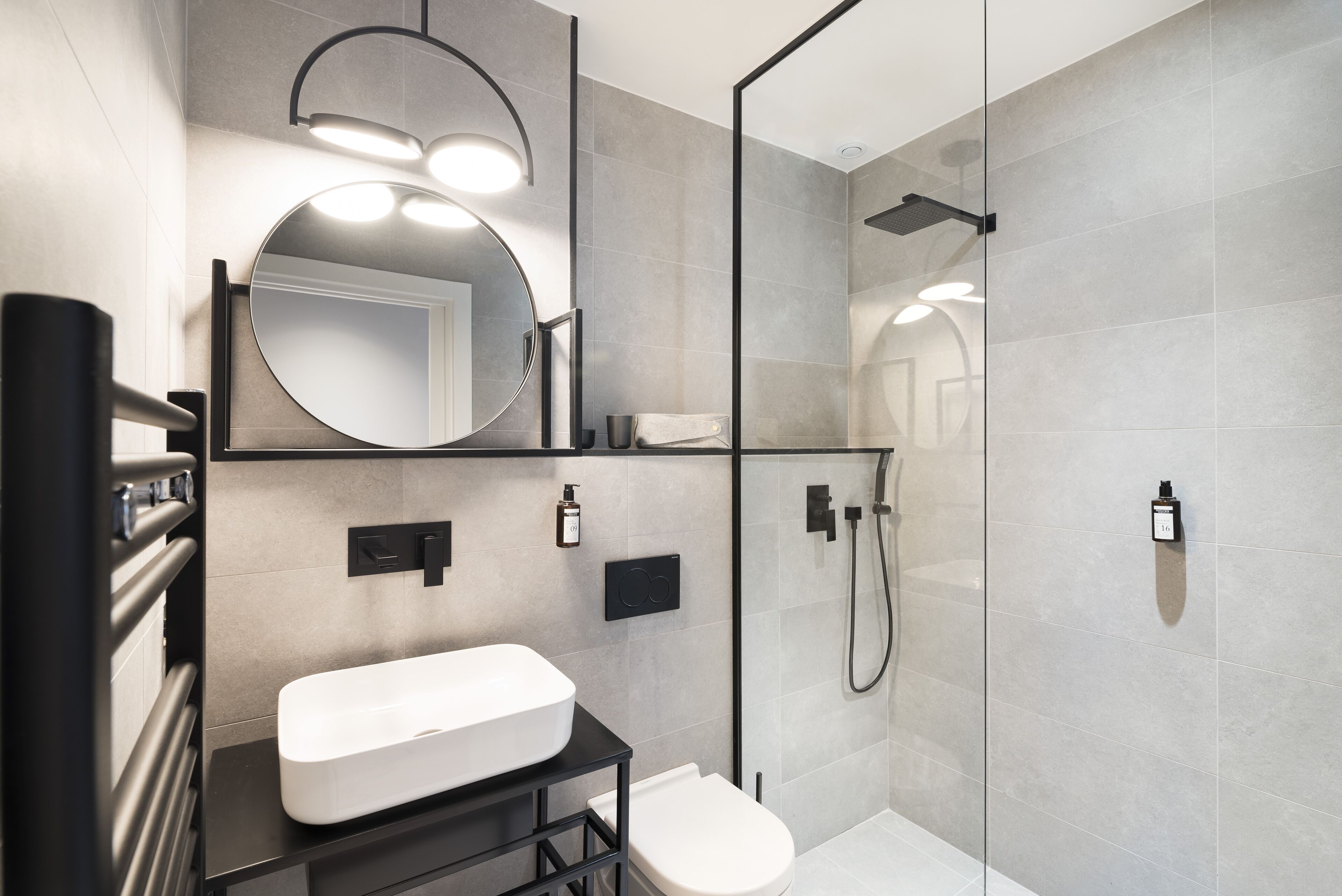 Une salle de bain moderne avec un lavabo blanc, un miroir rond et une douche séparée par des parois en verre.
