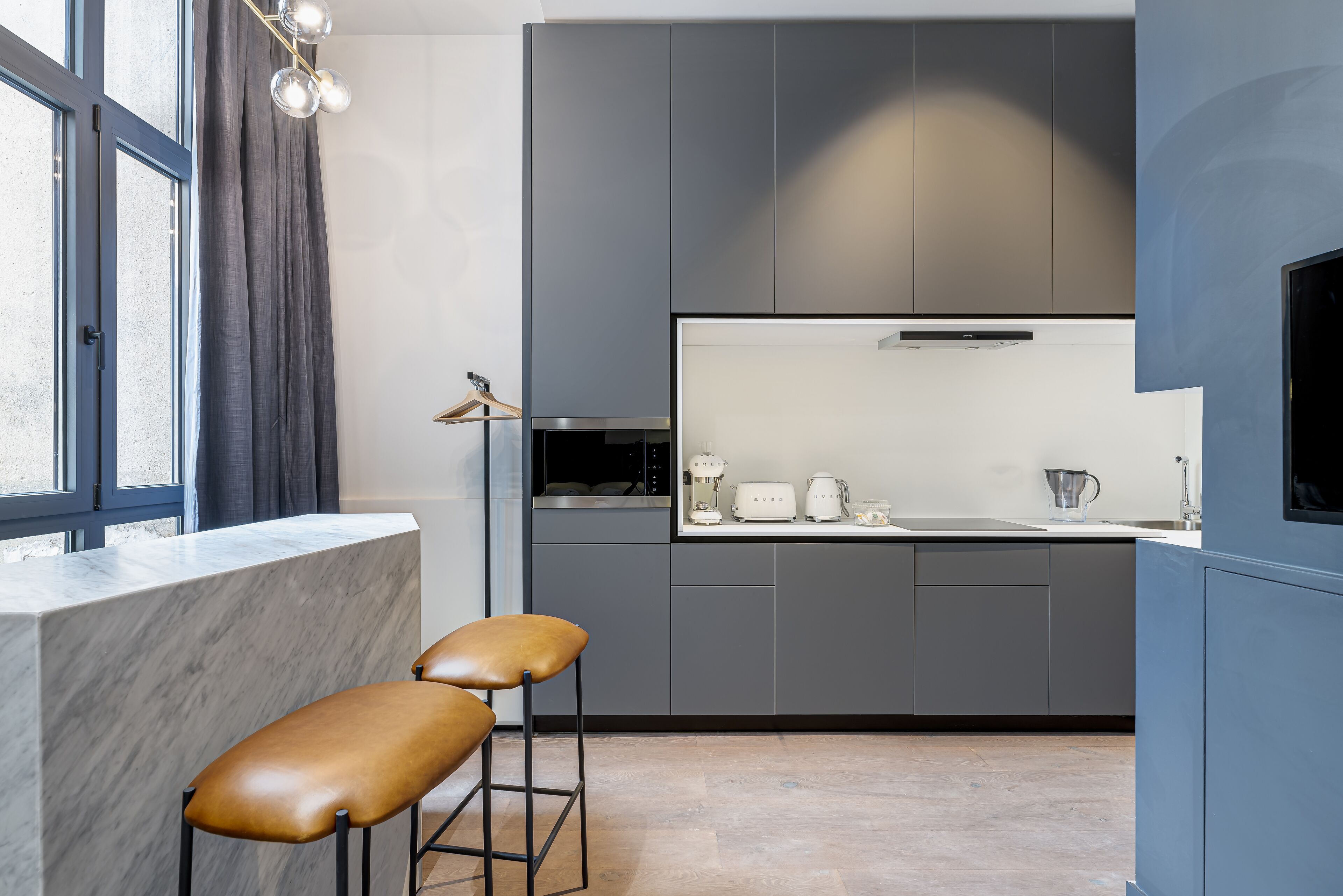 A modern kitchen with grey cabinets, a marble countertop, and two bar stools.