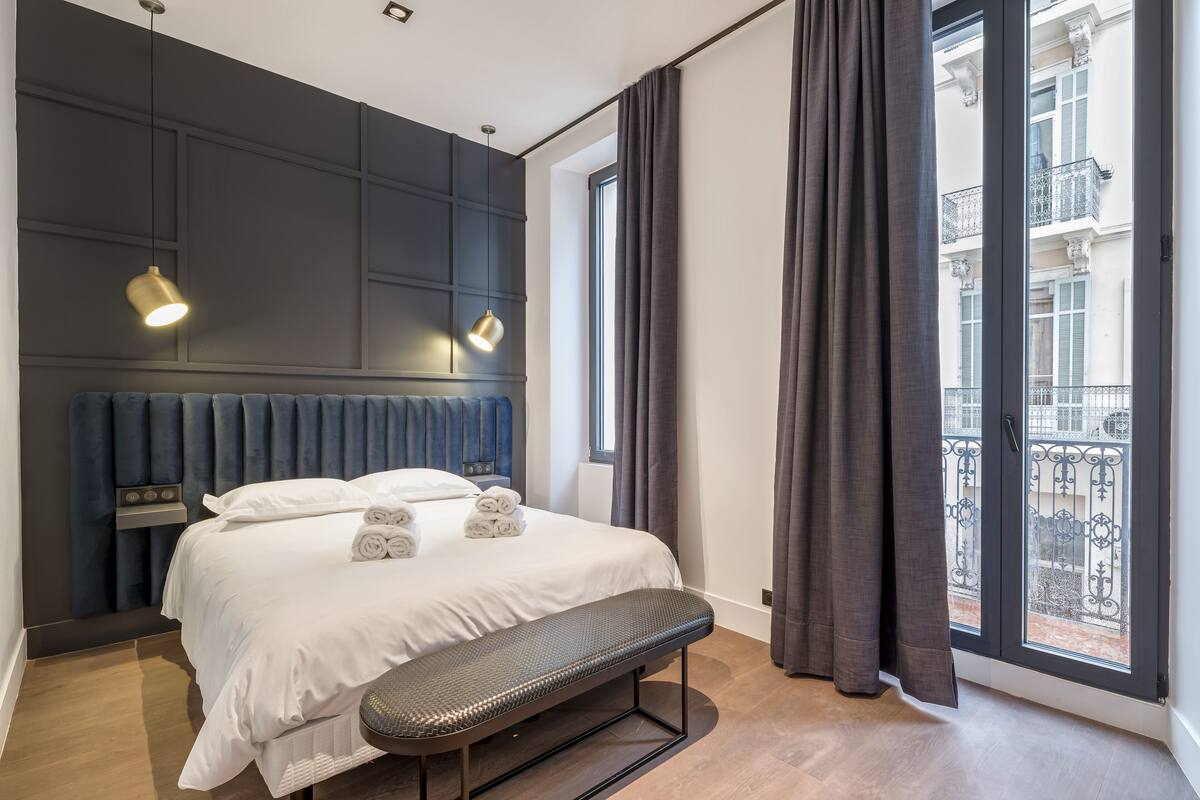 A modern bedroom with a large bed, a bench, and a view of the city through a large window.