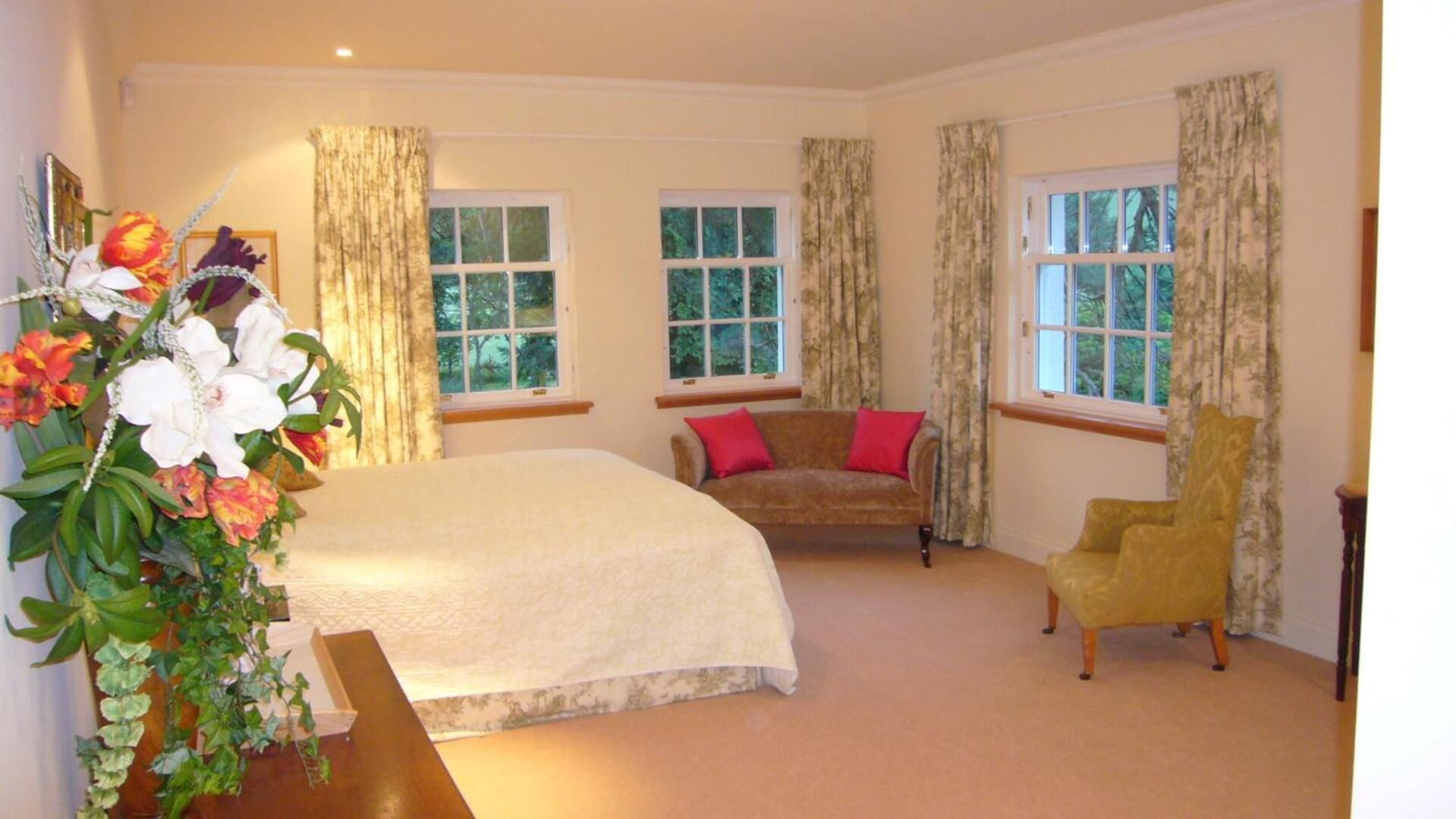 A bedroom with a large bed, two windows, a sofa, a chair, and a plant.