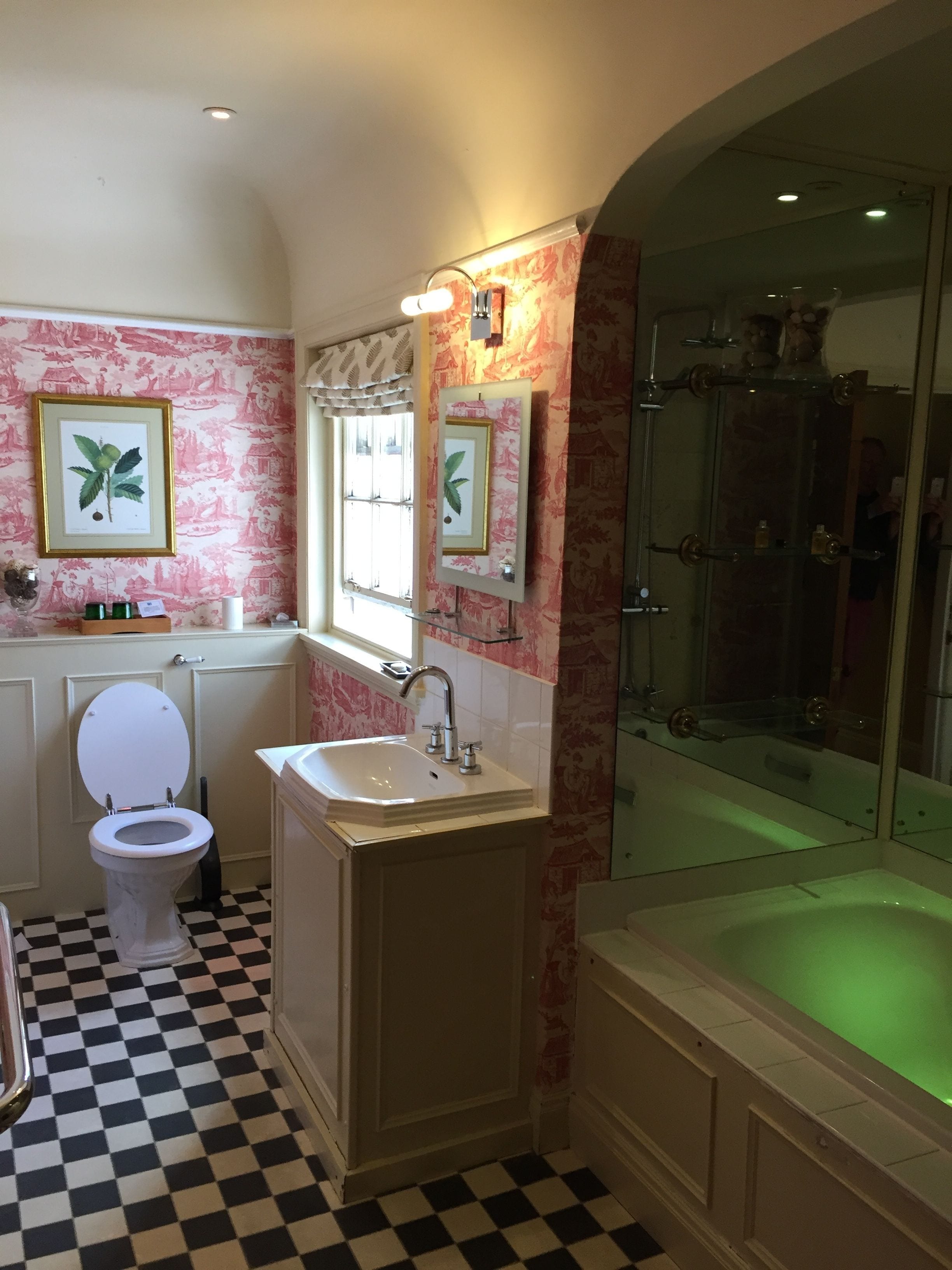 Un baño con piso a cuadros, un inodoro blanco, un lavamanos, un espejo y una ducha con cerramiento de vidrio.