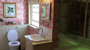 Un baño con piso a cuadros, un inodoro blanco, un lavamanos, un espejo y una ducha con cerramiento de vidrio.