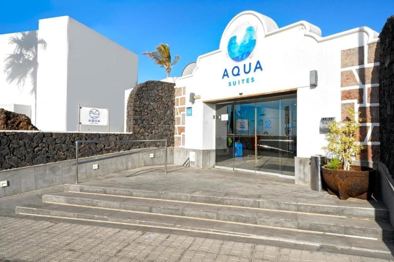 A building with a sign reading "AQUA SUITES" and a stone wall.